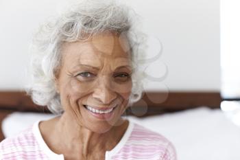Head And Shoulders Portrait Of Smiling Senior Woman Sitting On Bed At Home Looking Positive