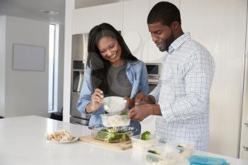 Couple In Kitchen Preparing High Protein Meal And Putting Portions Into Plastic Containers