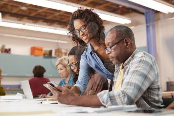 Teacher Helping Retired Senior Man Attending IT Class In Community Centre