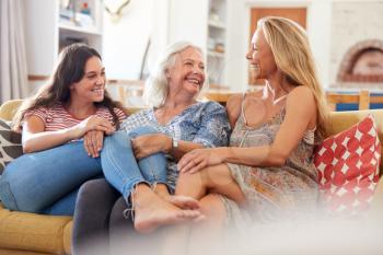 Mother With Adult Daughter And Teenage Granddaughter Relaxing On Sofa And Talking At Home