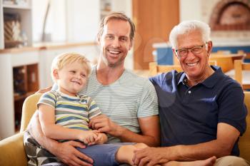 Portrait Of Father With Adult Son And Teenage Grandson Relaxing On Sofa And Talking At Home