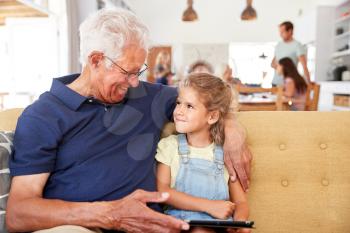 Grandfather Sitting With Granddaughter On Sofa Using Digital Tablet At Home