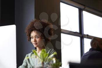 Millennial black female creative sitting at a desk in an office using a computer, close up