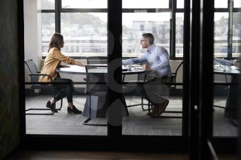 A businessman and young woman meeting for a job interview, full length, seen through glass wall