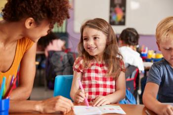 Elementary School Teacher Giving Female Pupil One To One Support In Classroom