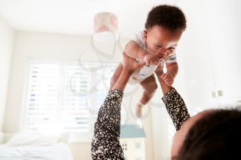 Proud Mother Cuddling Baby Son In Nursery At Home