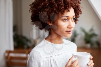 Young Woman Relaxing In Loft Apartment With Hot Drink