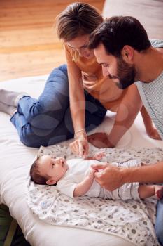 Loving Parents With Newborn Baby Lying On Bed At Home In Loft Apartment