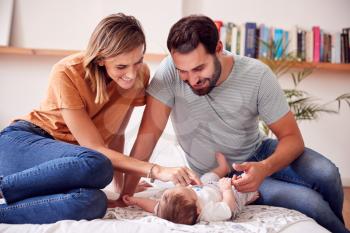 Loving Parents With Newborn Baby Lying On Bed At Home In Loft Apartment