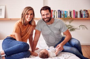 Portrait Of Loving Parents With Newborn Baby Lying On Bed At Home In Loft Apartment