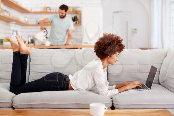 Woman Relaxing Lying On Sofa At Home Looking At Laptop
