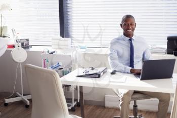 Portrait Of Smiling Male Doctor Sitting Behind Desk In Office