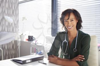 Portrait Of Smiling Female Doctor With Stethoscope Sitting Behind Desk In Office