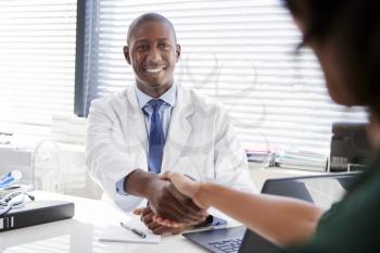 Female Patient Shaking Hands With Doctor Sitting At Desk In Office