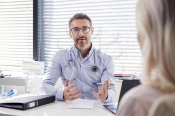 Mature Female Patient In Consultation With Doctor Sitting At Desk In Office