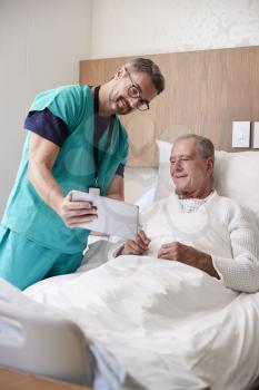 Surgeon With Digital Tablet Visiting Senior Male Patient In Hospital Bed In Geriatric Unit