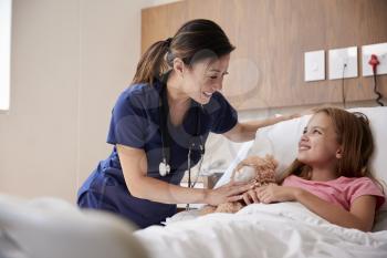 Female Nurse Visiting Girl Lying In Hospital Bed Hugging Teddy Bear