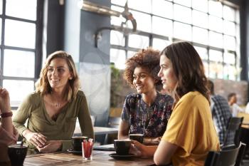 Three Young Female Friends Meeting Sit At Table In Coffee Shop And Talk