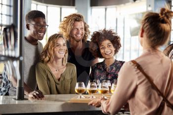 Waitress Serving Group Of Friends Beer Tasting In Bar