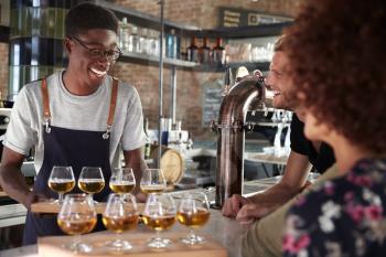 Waiter Serving Group Of Friends Beer Tasting In Bar