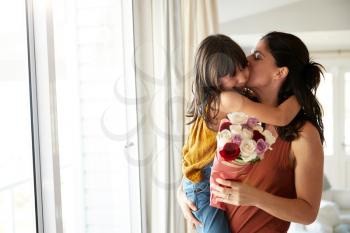 Mid adult woman holding her daughter, who’s given her a bunch of flowers on her birthday, waist up