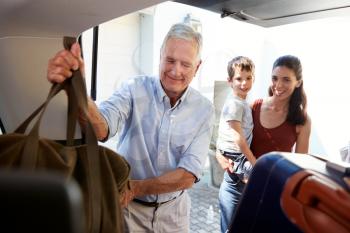 Senior white man packing car boot with holiday luggage, watched by his adult daughter and grandson