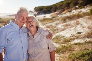 Senior white couple standing on a beach embracing and smiling to camera, close up