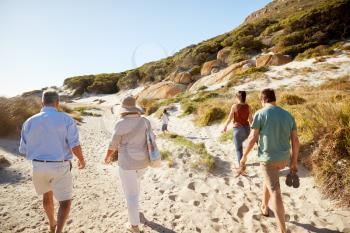 Parents and grandparents walking on beach with young boy running ahead of them