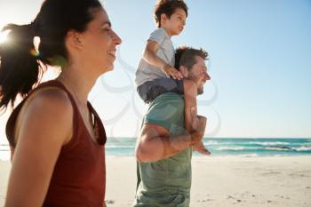 Mid adult white couple walking on a beach, dad carrying son on his shoulders, side view, close up