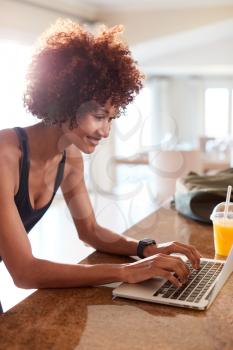 Millennial African American woman using laptop to check fitness data after her work out, vertical