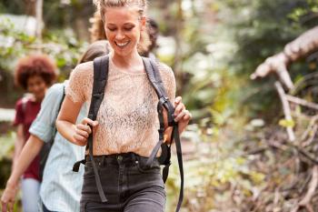 Millennial white woman hiking on a forest trail with friends, close up, front view