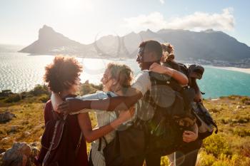 Millennial friends on a hiking trip embrace at the summit to celebrate their climb, back view