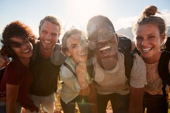 Young adult friends on a hike celebrate reaching the summit, smiling to camera, close up