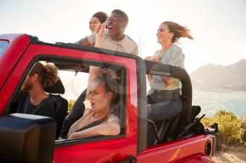 Five young adult friends on a road trip driving in an open top jeep by the sea