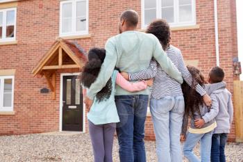 Rear View Of Family Standing Outside New Home On Moving Day Looking At House