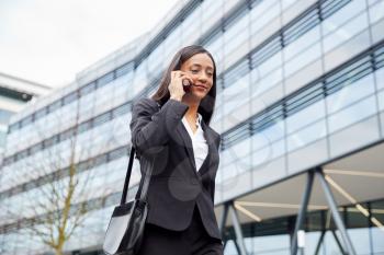 Businesswoman Commuting To Work Talking On Mobile Phone Outside Modern Office Building