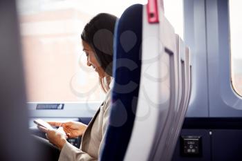 Businesswoman Sitting In Train Commuting To Work Checking Messages On Mobile Phone