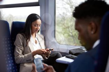 Business Passengers Sitting In Train Commuting To Work Looking At Mobile Phones