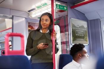 Female Passenger Standing By Doors In Train Using Mobile Phone