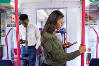 Business Passengers Standing In Train Commuting To Work Looking At Mobile Phones