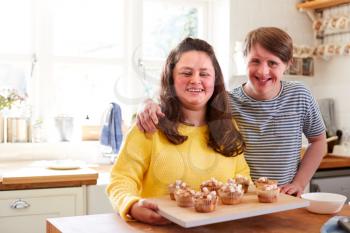 Portrait Of Downs Syndrome Couple Decorating Homemade Cupcakes With Marshmallows In Kitchen At Home