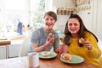 Portrait Of Young Downs Syndrome Couple Enjoying Tea And Cake In Kitchen At Home