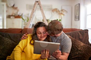 Loving Young Downs Syndrome Couple Sitting On Sofa Using Digital Tablet At Home