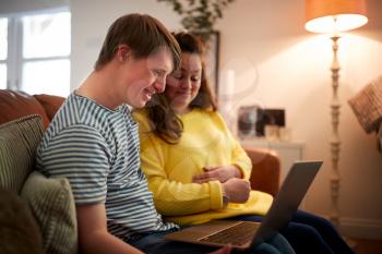 Young Downs Syndrome Couple Sitting On Sofa Using Laptop At Home