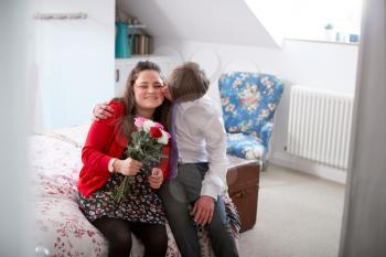 Loving Young Downs Syndrome Couple Sitting On Bed With Man Giving Woman Flowers