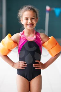 Portrait Of Girl Wearing Armbands Standing By Edge Of Swimming Pool Ready For Lesson