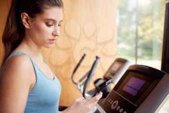 Woman Exercising On Treadmill At Home Checking Fitness App On Mobile Phone