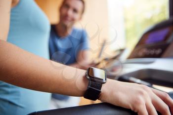 Woman In Gym With Personal Trainer Analysing Performance Using Smart Watch And Digital Tablet