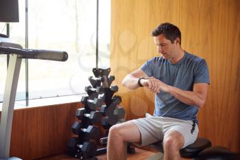 Man Exercising Sitting On Weight Bench In Home Gym Checking Smart Watch