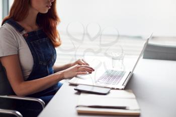 Close Up Of Casually Dressed Young Businesswoman Working On Laptop At Desk In Modern Workplace